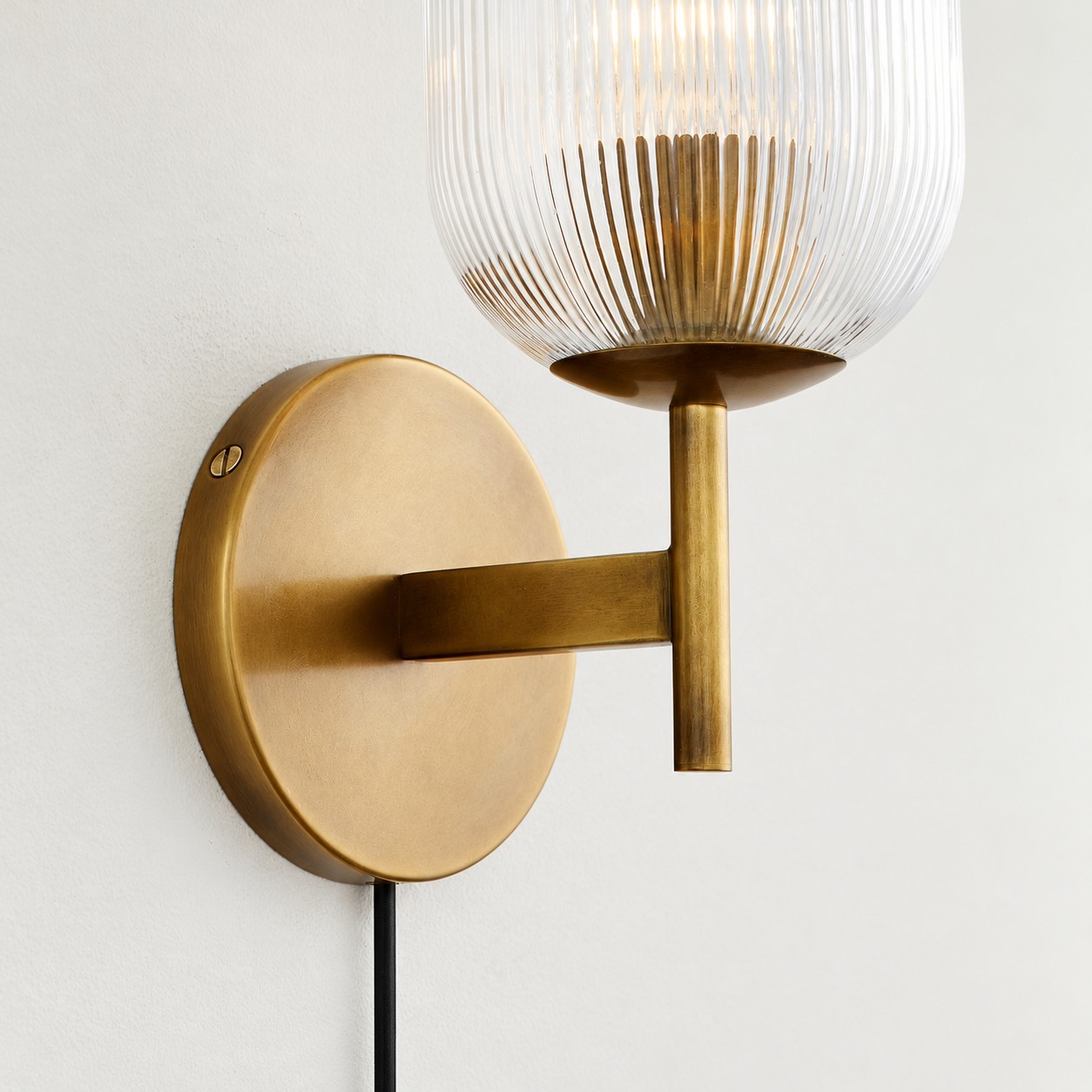Close view of the ribbed glass shade, brass arm and plug-in cord